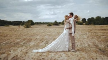 Loving bride and groom embrace together facing each other, beautiful couple in the countryside, Bride in boho dress and groom in suit standing across the field medium shot, slow motion. High quality