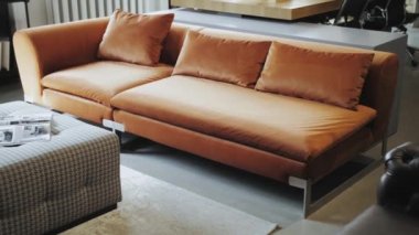 No people dolly shot of cozy loft style office interior with natural lighting, the puff furniture is lined with checkered fabric, a magazine is placed on it as a decoration and orange sofa.4k