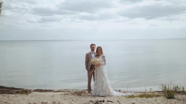 美しい新婚カップルのカメラにポーズを 海の背景には スローモーションです 愛の花嫁と新郎のビデオ肖像画 高品質4K映像 — ストック動画