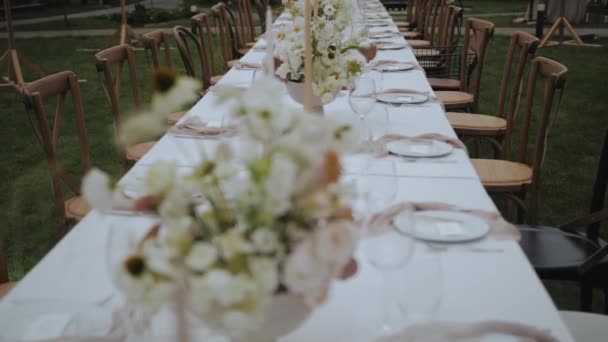 パステルカラーの新鮮な花や緑 お祝いのプレートやワイングラスの花束の花瓶と結婚式の装飾されたディナーテーブルのドリーショット テーブルの上の花の組成 スローモーション 4K映像 — ストック動画