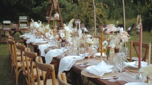 木製の椅子や結婚式のテーブルの屋外のキャンドルで飾られ 乾燥したショットや宝の花のブーブースタイルの結婚式のディナー プレートやワイングラスのために 遅い動きを撮影した 4K映像 — ストック動画