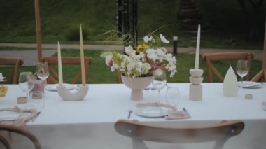 Pastel yaban çiçekleri, mumlar, küçük rahat düğün partisinde eski moda sandalyeler, arka planda yeşil çimenler, yavaş çekim. Yüksek kalite 4k görüntü