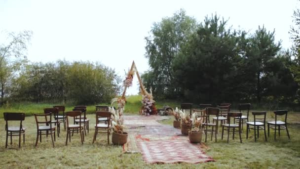 屋外の結婚式で豪華なボヘミアンアーチの装飾を撮影しました パステルカラー ドライフラワー 木製の椅子や昔ながらのカーペットの花の組成物 夏の結婚式 — ストック動画