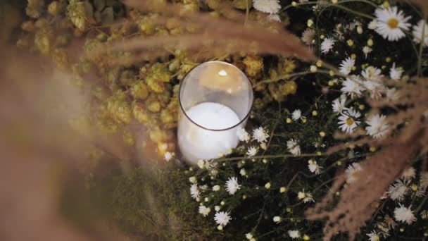 精美的花卉装饰与燃烧的蜡烛的特写 玻璃瓶中的蜡烛立在绿色苔藓和雏菊上 节日装饰用浆糊色 慢镜头拍摄 高质量的4K镜头 — 图库视频影像