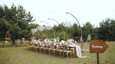 Dışarıda mumlarla süslenmiş ve kurutulmuş düğün masası, boho tarzı düğün yemeği için pastel çiçekler, tabaklar ve şarap bardakları, ön planda ağır çekimde kelime seremonisiyle yazılmış yazıtlar. 4k 