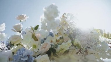  Çiçekler, güller, beyaz ve mavi renkte kasımpatılar, çiçekler arasında güneş ışınları, düğün seremonisi dışında yavaş çekimde parlıyor. Yüksek kalite 4k görüntü