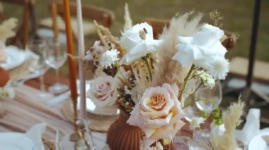 Çok güzel bir buket gül ve kurutulmuş çiçekler servis edilen masanın üzerinde ve mumlarla süslenmiş boho tarzı düğün yemeği, tabaklar ve şarap bardakları, vurulan yok. Yüksek kalite 4k görüntü