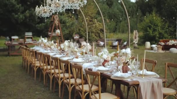 キャンドルやブーホスタイルの結婚式のディナー プレートやワイングラスのための乾燥パステルの花で飾られたウェディングテーブルの屋外 風がテーブルクロス ナプキンや花の組成を振る — ストック動画