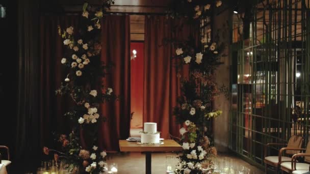 レストランでの結婚式のアーチの近くの木製のテーブルの上に緑の小枝で飾られた美しい結婚式のケーキ スローモーション 高品質4K映像 — ストック動画