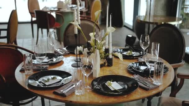 美しい結婚式の装飾は すべて黒と白の色で飾られ カメラはテーブルの周りに遅い動きを移動します 柔らかい花の美しい黒いプレート キャンドル テーブルの上のワイングラス — ストック動画
