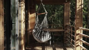 Kapalı bir hamak, gün batımında ahşap bir terasta, gün batımında tahta zeminde, çam ormanı arka planında, kamera yavaş çekimde sallanıyor. Yüksek kalite 4k görüntü