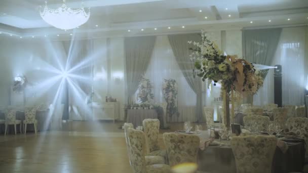 stock video Wedding tables decoration with big floral composition, served plates and glasses. Light rays through the banquet hall. All decorated in pastel colors, camera moving slow motion. 4k