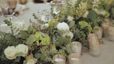 Beyaz çiçekler ve yeşilliklerle süslenmiş yakın plan düğün masası süslemeleri mumlu bir düğün için güzel çiçek düzenlemeleri, yavaş çekim. Yüksek kalite 4k görüntü