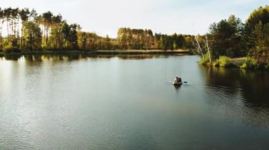 Gölün ortasındaki bir teknede tanınmayan insanlar. Gölün çam ağaçlarıyla kaplı küçük bir adanın havadan görünüşü. Adanın yakın çekim görüntüsü. Yüksek kalite 4k görüntü