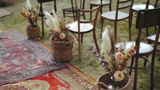 さまざまな花 乾燥して新鮮な花束のハンドヘルドショットは 木製の椅子と芝生の上で昔ながらのカーペットの近くのウィッカーバスケットに立って 屋外の結婚式で美しい装飾 — ストック動画