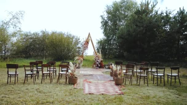 屋外の結婚式で豪華なボヘミアンアーチの装飾を撮影しました パステルカラー ドライフラワー 木製の椅子や昔ながらのカーペットの花の組成物 夏の結婚式 — ストック動画