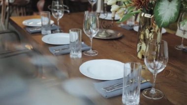 Yakın plan güzel bir düğün dekoru kompozisyonu masanın üzerinde, açık olan avizeler masanın üzerinde asılı. Beyaz tabaklar, mumlar, masada şarap bardakları, ağır çekim. Yüksek kalite 4k görüntü