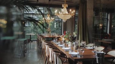 Masanın üzerinde güzel bir düğün dekoru çiçek kompozisyonu açık avizeler masanın üzerinde asılı. Beyaz tabaklar, mumlar, masada şarap bardakları, ağır çekim. Yüksek kalite 4k görüntü