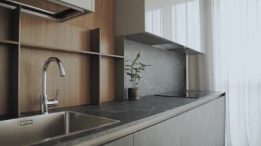 Mutfak lavabosu ve musluğu, içi bitkilerle dolu. Basit bir modern mutfak tasarımı. Duvarda siyah seramik fayanslar ve tezgah ve ahşap cephe, yavaş çekim. 4k görüntü