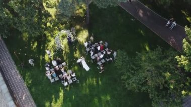 Beyaz çiçeklerle süslenmiş parktaki düğün töreninin havadan görünüşü ve konuklar damadın yanına giderken gelini alkışlıyorlar, tanınmaz haldeler. 4k görüntü
