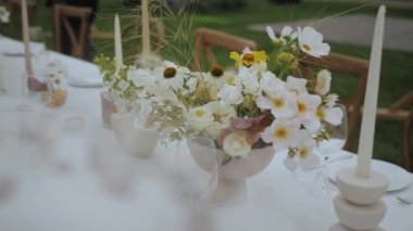 Close-up decorated dinner table with a vase of bouquet of pastel fresh flowers and greens. Floral composition from a fresh bouquet for a wedding event, blured, slow motion. High quality 4k footage