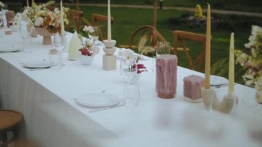Pastel çiçekler, mumlar, eski moda sandalyeler ve küçük düğün partisinde arka planda eski moda lambalar olan yakın plan düğün masası ayarı, yavaş çekim. Yüksek kalite 4k görüntü