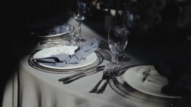 Yakın plan düğün masası dekorasyonu: servis tabakları, masada bardaklar, tabakta güneş ışığı ışınları, masada mavi peçete. Şenlikli masa dekoru, hepsi pastel mavi renklerle süslenmiş, yavaş hareket eden 45 'lik. 
