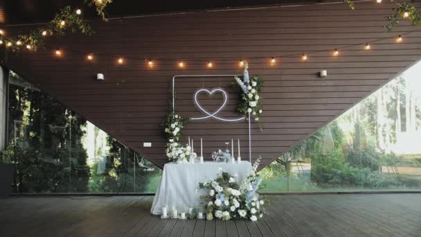 花嫁とグロムのための美しい結婚式のテーブルの装飾 すべてパステルブルーの色で装飾されています お祝いの背景として木の壁に掛かるネオンハートの装飾は テーブルの花嫁とグルメを提供しました 4K映像について — ストック動画