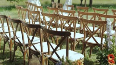 Dışarıda, ağaçların arasında parkta bir düğün töreni. Beyaz yastıklı ahşap sandalyeler, ağır çekimde. - Evet. Yüksek kalite 4k görüntü