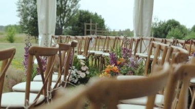 Üzerinde beyaz yastıklar olan bir sürü tahta sandalye ve güzel çiçekli kompozisyon. Dışarıda, parkta, ağaçların arasında, yavaş çekim. - Evet. Yüksek kalite 4k görüntü