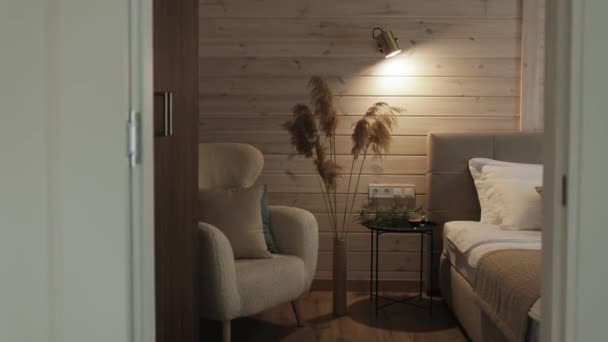柔らかい椅子 ベッド 木の壁の暖かいランプ ライトが付いている居心地のよい寝室 インテリアの装飾として背の高い花瓶のパンプス草 小さな家のカメラの居心地の良い部屋が前進します 高品質の4K映像 — ストック動画