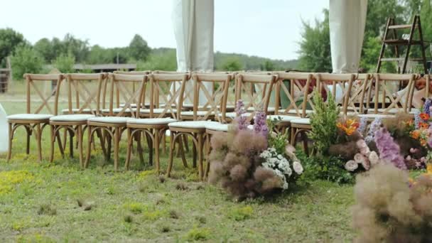 フロントビューには白い枕と美しい花の構成を持つ多くの木製の椅子があります 木々の間の公園の外の結婚式 ゆっくりとした動き 高品質の4K映像 — ストック動画