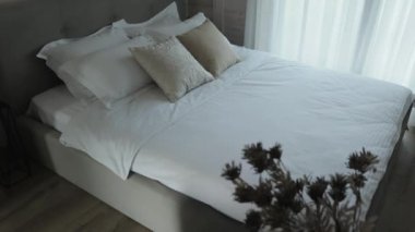 Modern yatak odasında beyaz çarşaflı yatak. Pencerenin yanında tüllü bir yatak. Ev dekorasyonu ve iç tasarım, çarşaf yıkama ve mobilya servisi, yavaş çekim. Yüksek kalite 4k görüntü