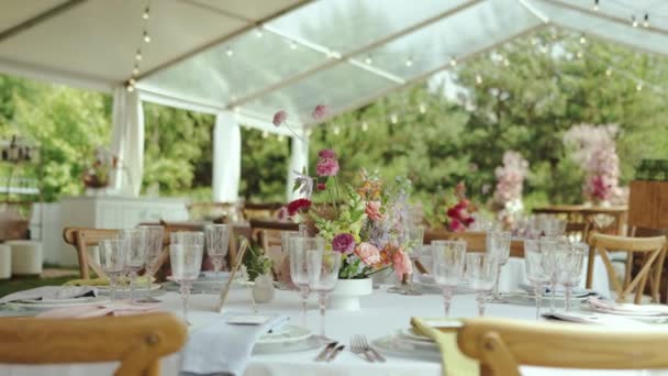 花の組成 ピンクのバラ 白いテーブルクロス 木製の椅子 ワイングラスとテーブルの上のプレートが付いている美しい装飾されたお祝いのテーブル 4Kについて — ストック動画