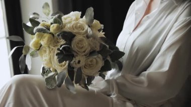 Yakından güzel bir buket, taze beyaz güller ve gelinin ellerinde yeşillik, otel odasında gelin sabahı, gelinin sabah bakışı yavaş çekim. Yüksek kalite 4k görüntü