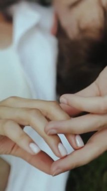 Dikey video meraklıları çimlere uzanıp nazikçe parmaklarına dokunurlar. Kadın eli erkeğin elinin üzerine uzanır, ellerle nazikçe dokunur. El ele tutuşun, ağır çekim. HD