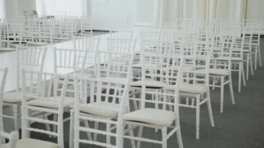 Many white chairs for guests. Wedding hall decoration in white color ready for guests with white color chairs and white floral composition. Wedding concept, slow motion. High quality 4k footage
