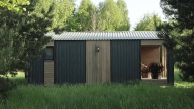 Ahşap teraslı küçük bir ev ve üzerinde sabah ormanında saklı iki sandalye, yeşil çimenler, ağaçların tepesinde güneş ışınları. Konforlu ahşap ev, ağır çekim. Yüksek kalite 4k görüntü