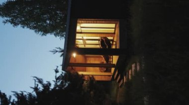 Çok yönlü bir video. Geceleri terastaki pencerelerden gelen sıcak elektrik ışığı ve sandalyeler. Gece evindeki ahşap İskandinavyalı pencerenin ışığı yanıyor. Ağır çekim. Yüksek kalite 4k görüntü