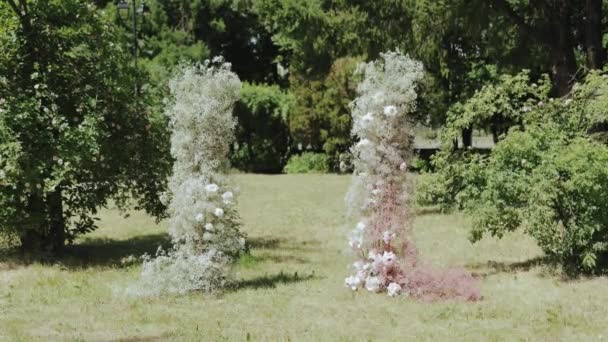 户外的婚礼在公园的树间举行 美丽娇嫩的婚纱拱形花冠 与吉普赛花冠 玫瑰粉色和白色 绿色草坪 缓慢移动 — 图库视频影像