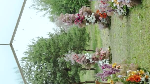 ヴァルティカルビデオ 美しくて柔らかい結婚式の花のアーチは 木々の間の公園の結婚式の外でピンクの花で飾られています スローモーション 高品質の映像 — ストック動画