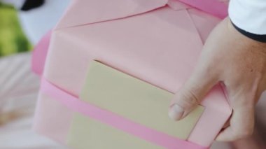 Yakın plan erkek el ele tutuşması hediyesi. Düğün hediyesi, doğum günü hediyesi. Hediye pembe bir kurdeleyle sarılmış pembe bir kağıda sarılmış. Yüksek kaliteli FullHD görüntüler