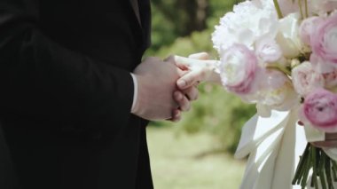 Yakından tanınmayan gelin ve damat törende el ele tutuşuyorlar. Gelin tutacağı buketi taze beyaz ve pembe güller. Yüzüklerimizi değiş tokuş ettikten sonra ayakta duran yeni evli çift. Yüksek kalite 4k görüntü