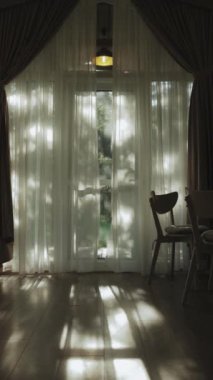 Masanın yanındaki ahşap sandalyeyle mutfak içi çekilen dikey video, sandalye ve ahşap zemindeki tüllerden güneş ışınları geçiyor. Samimi iç tasarım. Yüksek kaliteli FullHD görüntüler