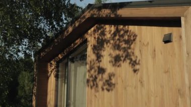 Arka planda ağaçlar olan ahşap bir kulübeye yakın plan, ahşap kaplamalı ve yeşil çimlerle çevrili kırsal kapılı büyüleyici bir cephe sergileniyor.