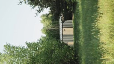 Çimenli bir tarlanın ortasında ağaçlarla çevrili küçük ahşap bir ev engin gökyüzünün altında doğal bir manzara yaratıyor. Dikey 