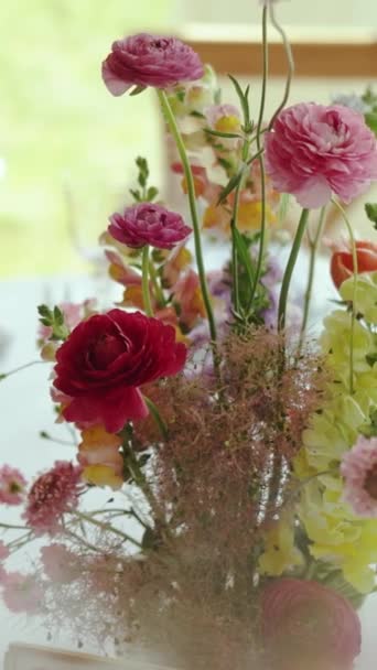 結婚式でテーブルの上の花とのクローズアップ美しい柔らかい構成 ピンク色の野生の花の花束は お祝いのテーブル ワイングラス プレート 屋外の結婚式にあります バーティカルビデオ — ストック動画