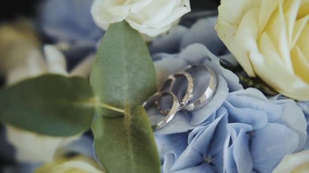 两个结婚戒指躺在一束生机勃勃的鲜花上 周围环绕着茂盛的陆生植物和青草 玫瑰花的电蓝色花瓣为这一浪漫事件增添了一丝色彩 — 图库视频影像
