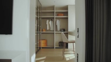 Kamera raflı soyunma odasına ilerlesin. Parlak giyinme odası, tuvalet masası ve rahat koltuğu olan modern gardırop, yavaş çekim. Yüksek kalite 4k görüntü