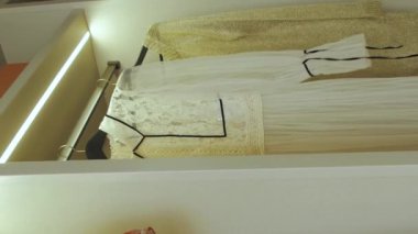 Raflı soyunma odası. Raflarda asılı duran yazlık elbiseler, öncü ışık gardırobu aydınlatıyor, yavaş çekim. Yüksek kalite 4k görüntü Dikey video